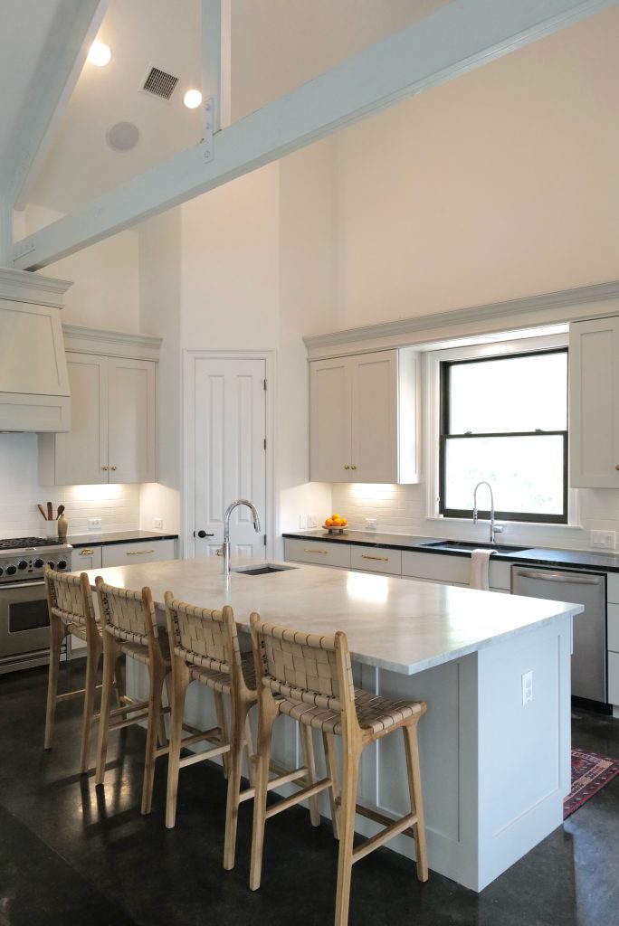White kitchen with a Taj Mahal quartzite island and woven counter stools