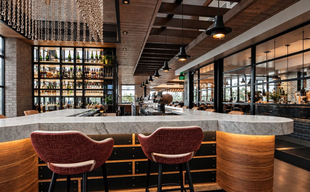 Restaurant bar with a curved Taj Mahal quartzite bar top and red upholstered stools
